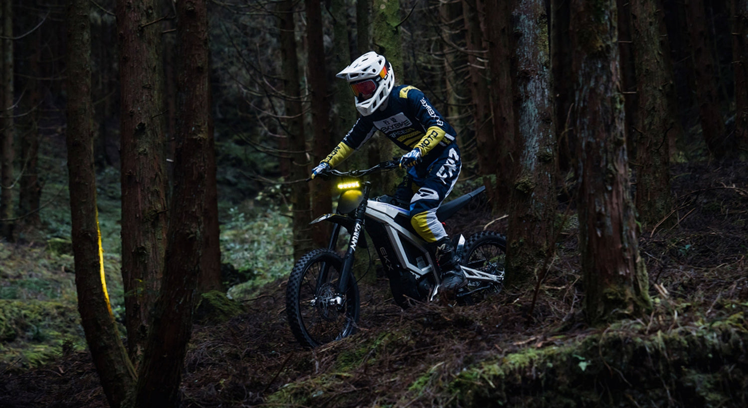 EKX M1 electric dirt bike riding through a pine forest, powered by a removable 72V 50Ah high-capacity lithium battery for long-range off-road performance.